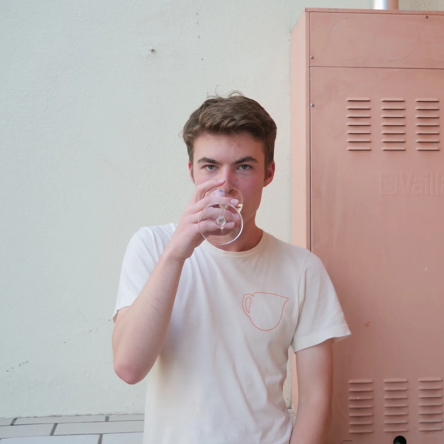 Me in white shirt outside on a balcony, staring into the camera while drinking wine